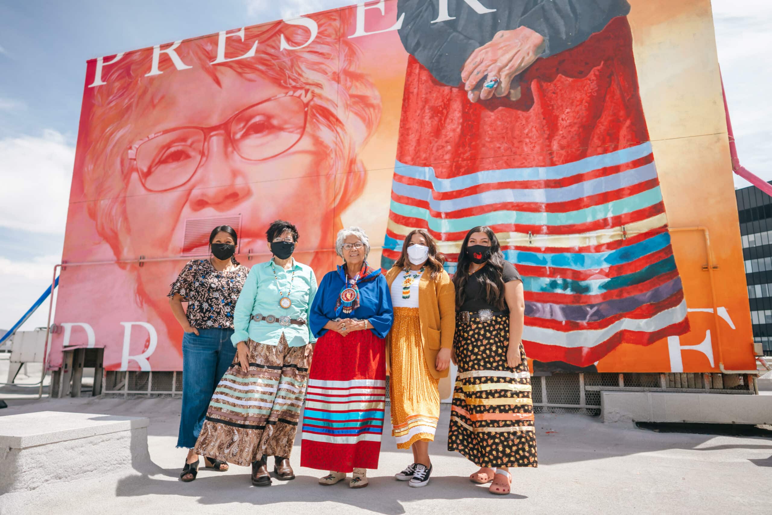 A photo of five women standing in front of a mural.