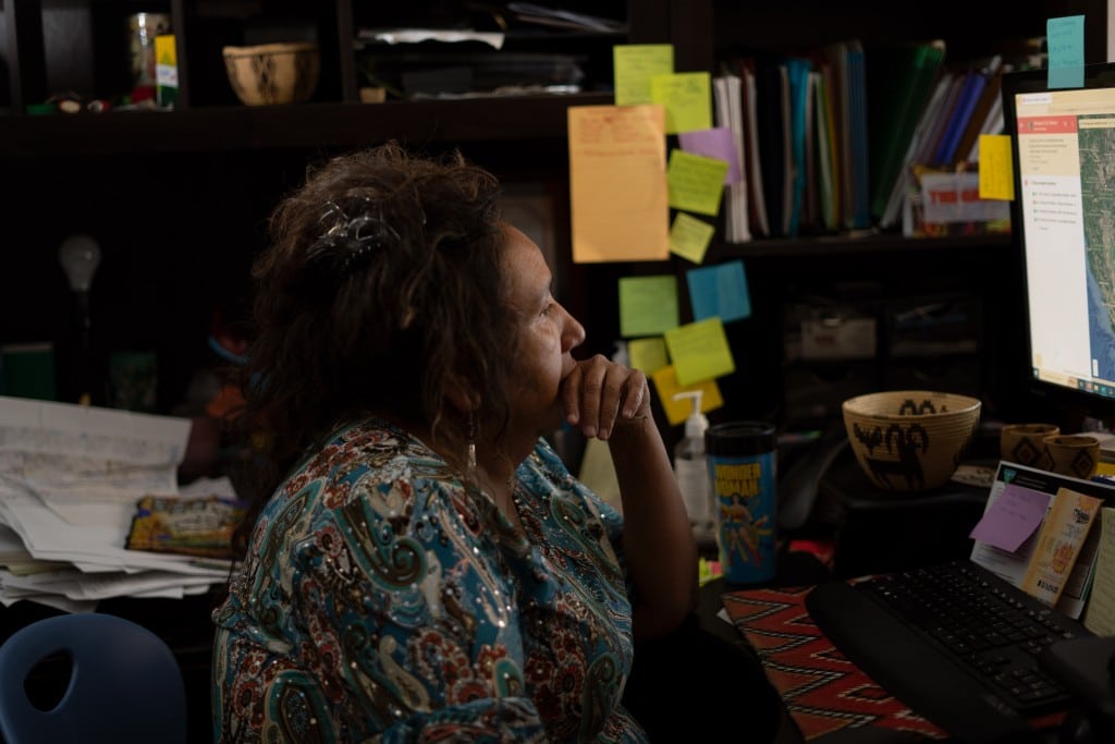 A photograph of a woman looking at a computer, in a dark room.