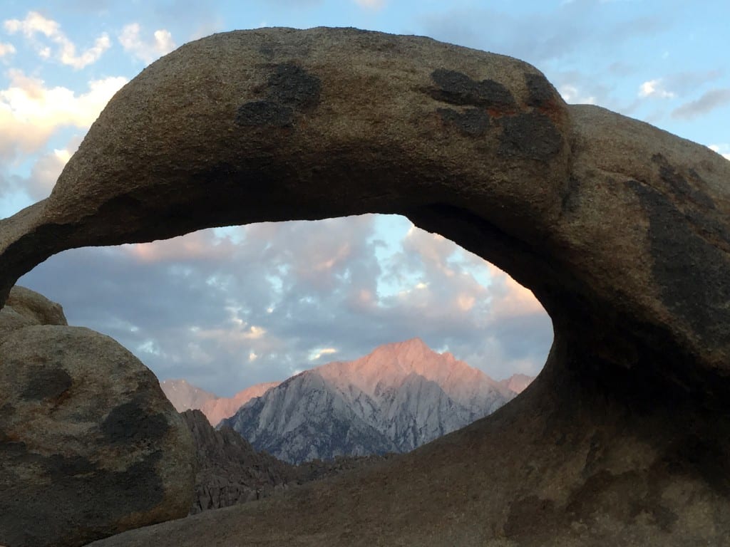 A photograph of a large rock arch, with a snow-capped mountain in the background.