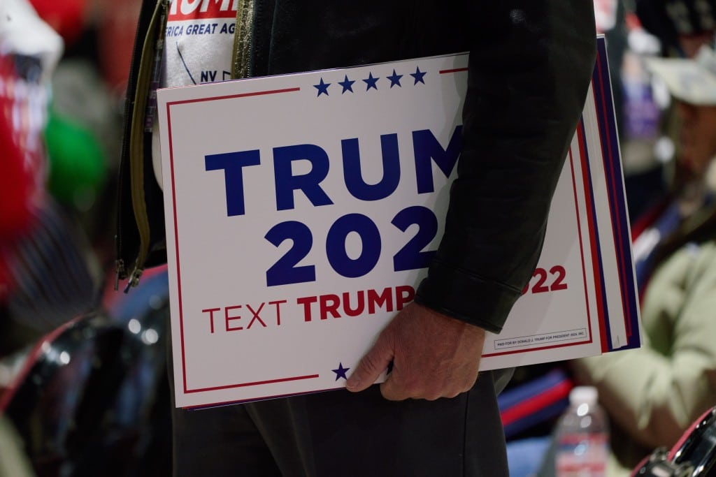 A photo of a man holding a white Trump 2024 sign.