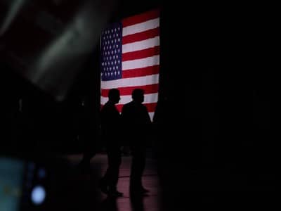 A photo of former president Donald Trump, as a silhouette, leaving the stage with a large American flag in the background.