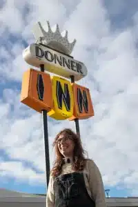A photo of artist Anna Newman standing in front of the Donner Inn motel sign